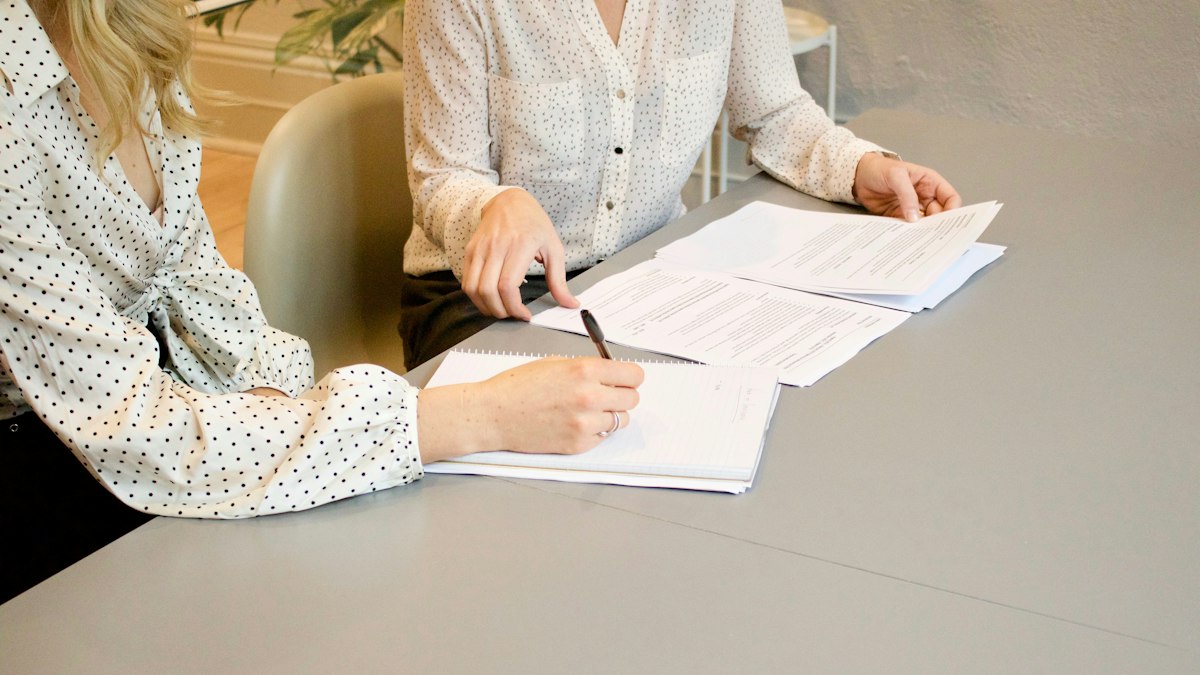 Two people signing paperwork across a desk