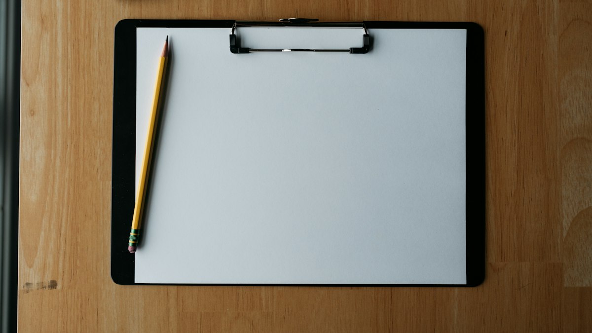 A blank clipboard and pencil on a wooden desk
