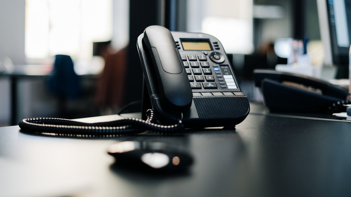 A black desk phone on a dark wooden table