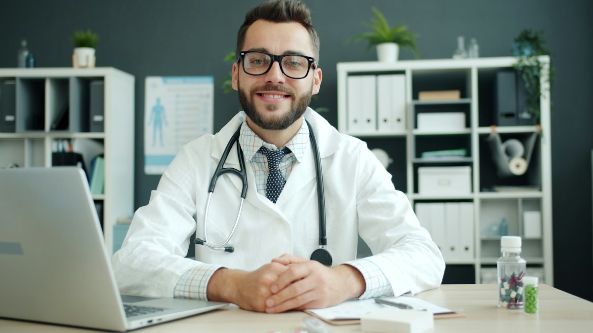 A doctor in a white coat with a stethoscope sitting at a desk